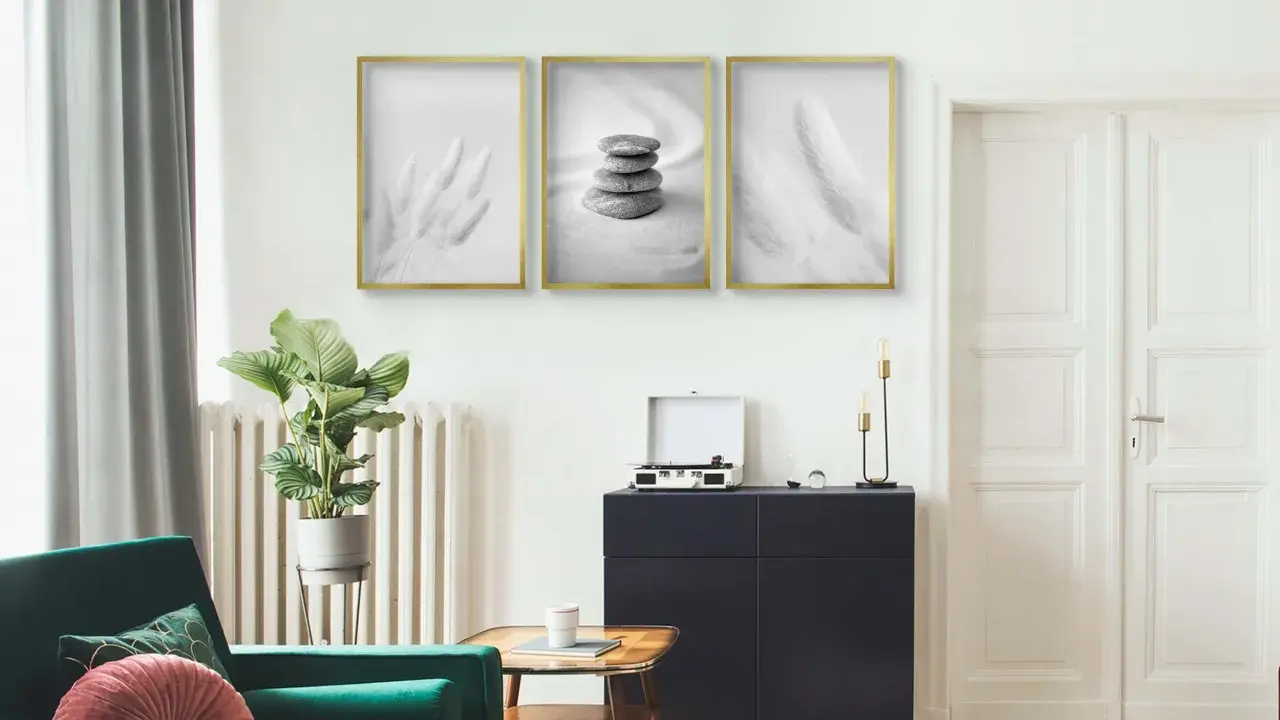 Trzy minimalistyczne plakaty w złotych ramach nad ciemną komodą. Dowiedz się, jak powiesić plakat bez niszczenia ścian.