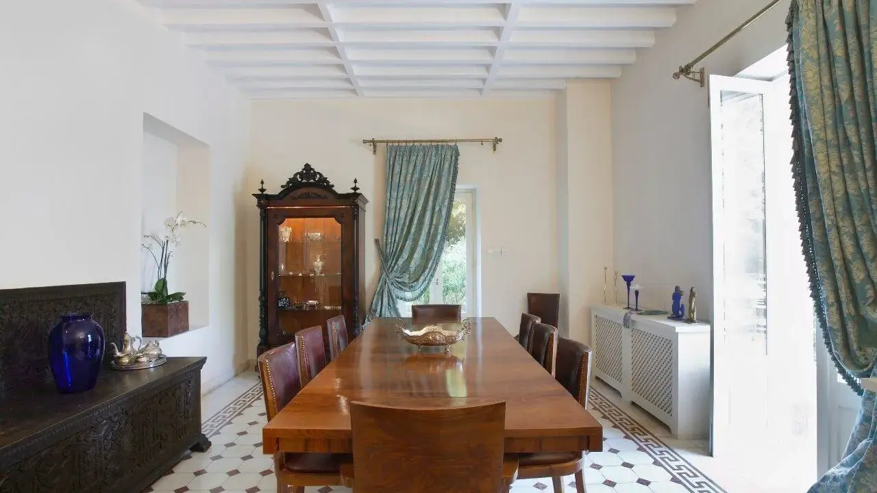 Elegancki salon w stylu kolonialnym z drewnianym stołem, witryną i zdobioną skrzynią.