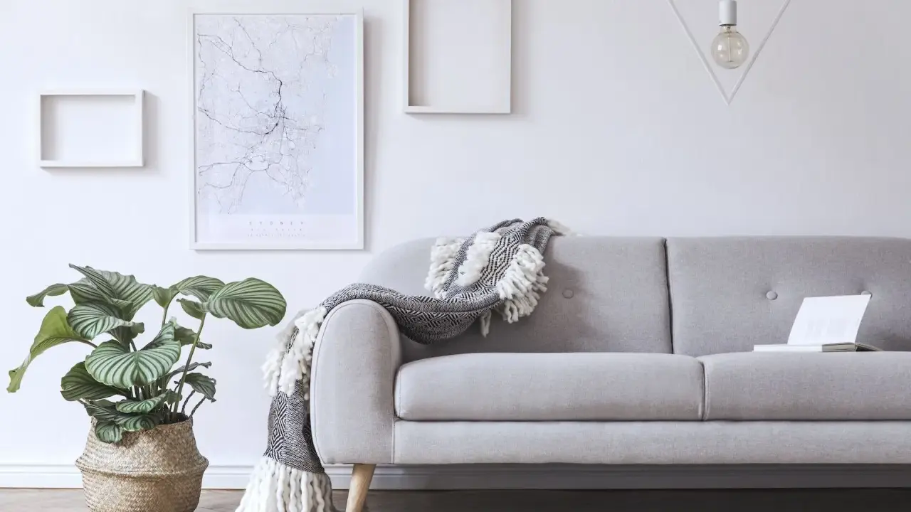 Przytulny salon z szarą kanapą, ozdobioną narzutą. Na ścianie mapa Sydney i geometryczna lampa.