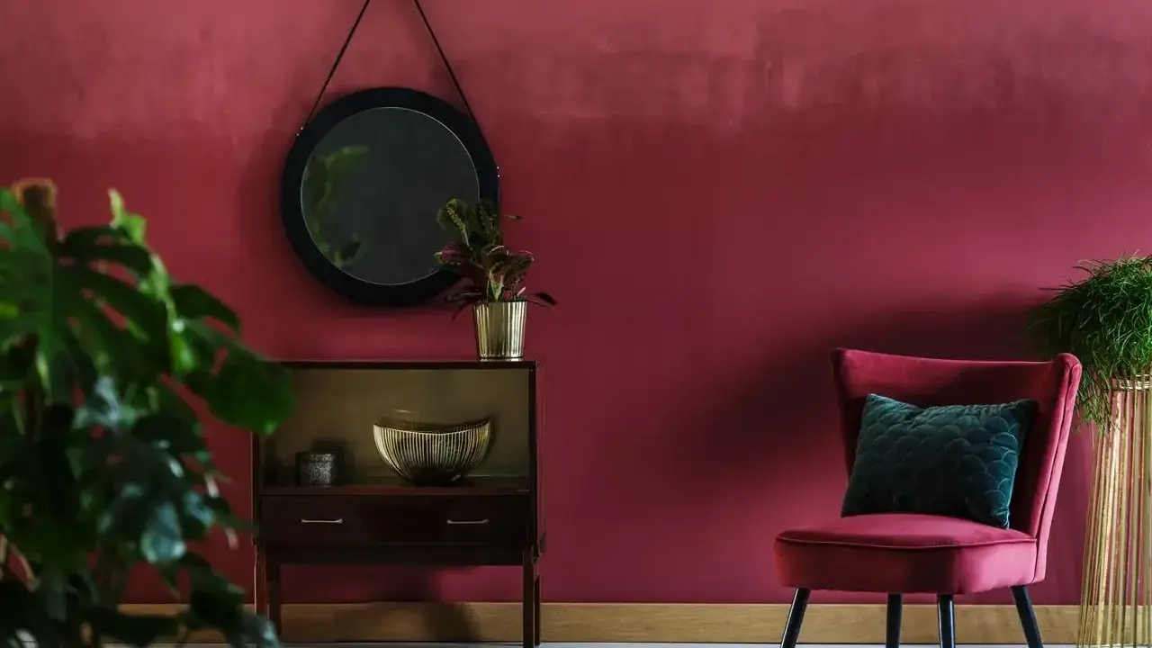 Elegancki salon z burgundowymi ścianami, aksamitnym fotelem i stylową komodą.