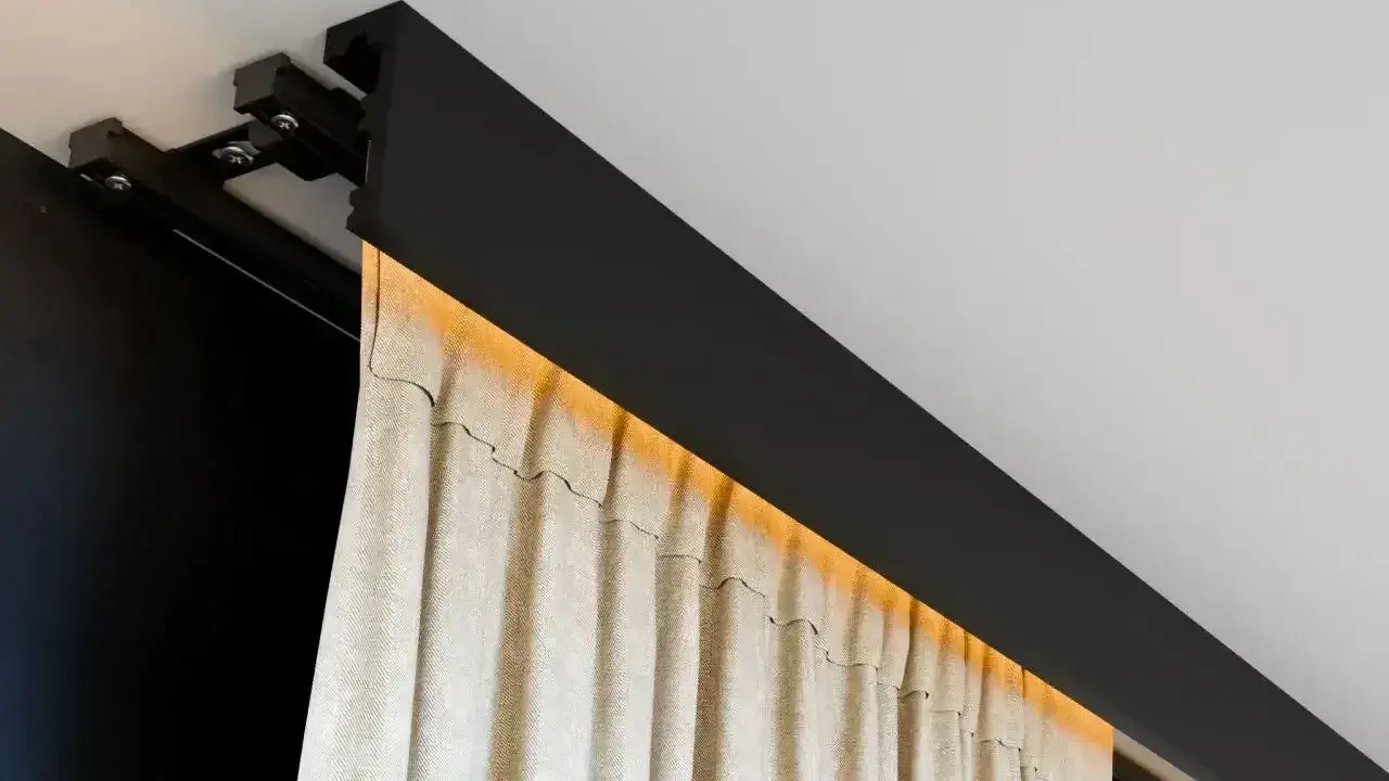 Nowoczesna szyna sufitowa z ukrytym oświetleniem LED, na której wiszą beżowe zasłony. Eleganckie rozwiązanie zamiast tradycyjnego karnisza.