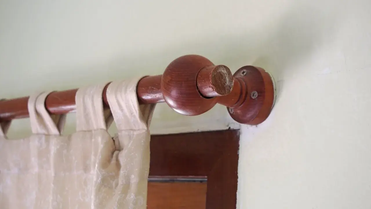 Drewniany karnisz z ozdobną kulą, zasłona w neutralnym kolorze. Karnisz inspiracje dla miłośników naturalnych materiałów.