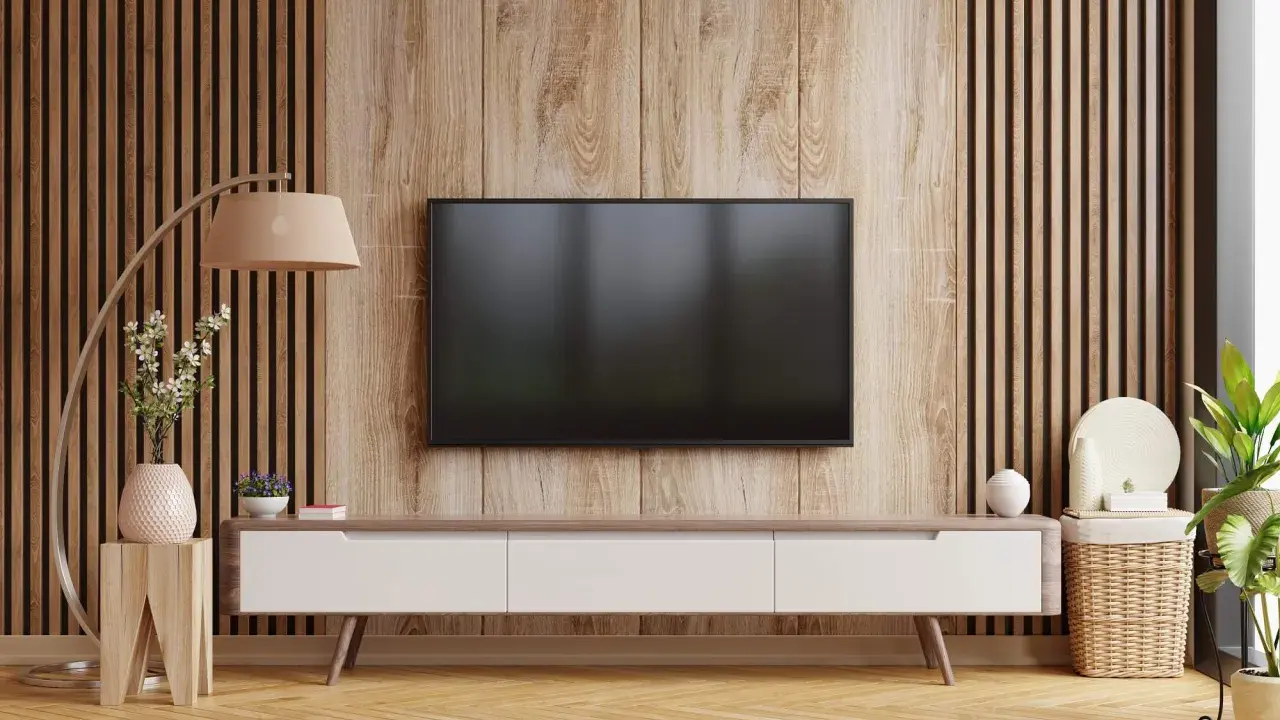 Nowoczesny salon z telewizorem na tle pionowych lamelek. Drewniana okładzina i meble tworzą przytulną atmosferę.