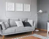 Szare wnętrze z kanapą, lampą i tryptykiem co to za styl? Abstrakcyjne rysunki psów na ścianie.