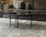 Miękki dywan w kolorze greige otula salon. Na nim dwa stoliki kawowe z marmurowymi blatami i aksamitna kanapa.