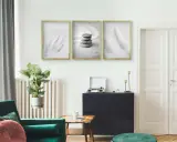 Trzy minimalistyczne plakaty w złotych ramach nad ciemną komodą. Dowiedz się, jak powiesić plakat bez niszczenia ścian.