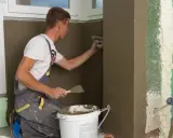 Budowlaniec tynkuje krzywą ścianę w przedpokoju.