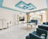 Nowoczesny salon z błękitnym, geometrycznym, dekoracyjnym malowidłem na suficie. Wygodne, granatowe sofy i białe meble tworzą elegancką przestrzeń.