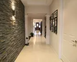 Nowoczesny korytarz z efektowną ścianą z kamienia, oświetloną kinkietem. Po prawej stronie galeria rodzinnych zdjęć.