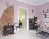 Pokój z ceglanym piecem i biurkiem, gdzie pracuje kobieta. Ściany w odcieniu **kolor lawendowy**.