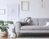 Przytulny salon z szarą kanapą, ozdobioną narzutą. Na ścianie mapa Sydney i geometryczna lampa.