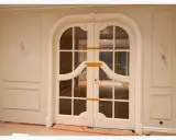 Elegancka sztukateria zdobi ściany korytarza, prowadząc do dwuskrzydłowych drzwi z łukiem i ozdobnymi szprosami.
