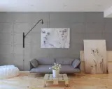 Nowoczesne wnętrze z panelami imitującymi beton. Sofa, stolik z palety, biały puf i obrazy tworzą stylową aranżację.