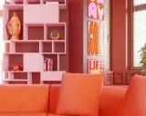 Pomarańczowa kanapa i różowe regały tworzą radosny, **dopamine decor**. Na półce figurka, telefon i zegar. Obok plakaty z napisami.