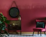 Elegancki salon z burgundowymi ścianami, aksamitnym fotelem i stylową komodą.