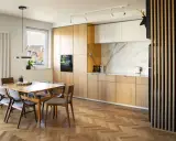Drewniane lamele w kuchni przy stole tworzą przytulną atmosferę. Jasne fronty szafek i marmurowy blat dodają elegancji.