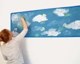 Kobieta maluje gąbką białe chmury na niebieskiej ścianie. Prosty sposób, jak namalować chmury na ścianie, tworząc niebo.