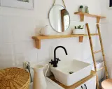 Urocza, mała łazienka w stylu retro z białymi kafelkami, drewnianymi półkami, okrągłym lustrem i bambusową drabiną.