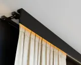 Nowoczesna szyna sufitowa z ukrytym oświetleniem LED, na której wiszą beżowe zasłony. Eleganckie rozwiązanie zamiast tradycyjnego karnisza.