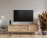 Nowoczesne aranżacje salonu z telewizorem na ścianie. Drewniana szafka RTV, lampa podłogowa i ozdobna roślina tworzą przytulną atmosferę.