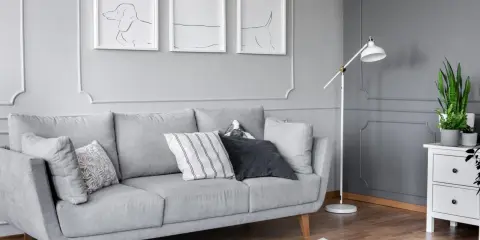 Szare wnętrze z kanapą, lampą i tryptykiem co to za styl? Abstrakcyjne rysunki psów na ścianie.