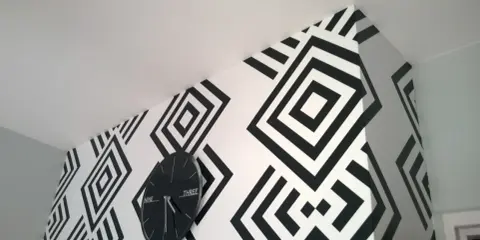 Nowoczesne tapety biało czarne z geometrycznym wzorem rombów. Zegar ścienny w czarnej ramie idealnie komponuje się z aranżacją.