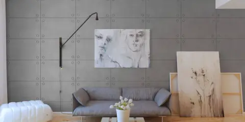 Nowoczesne wnętrze z panelami imitującymi beton. Sofa, stolik z palety, biały puf i obrazy tworzą stylową aranżację.