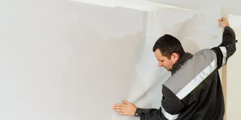 Mężczyzna przykleja tapetę. Czy kłaść gładź pod tapetę? To pytanie często zadawane przed remontem.