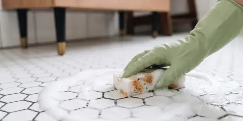 Rękawiczka w zielonej rękawicy czyści pianę na białych płytkach heksagonalnych. Dowiedz się, czym myć płytki, żeby nie było smug.