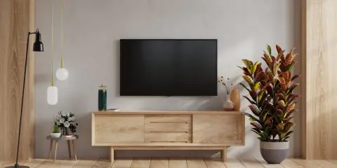 Nowoczesne aranżacje salonu z telewizorem na ścianie. Drewniana szafka RTV, lampa podłogowa i ozdobna roślina tworzą przytulną atmosferę.