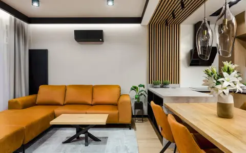 Nowoczesny salon bez sufitu z pomarańczową kanapą, drewnianym stołem i designerskimi lampami.