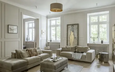 Elegancki salon z dwoma beżowymi sofami, ozdobną sztukaterią na ścianach i dużym obrazem.
