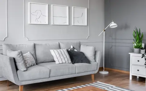 Szare wnętrze z kanapą, lampą i tryptykiem co to za styl? Abstrakcyjne rysunki psów na ścianie.