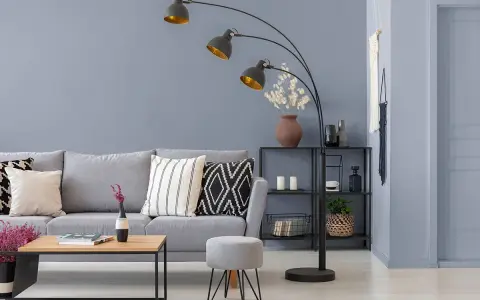 Przytulny salon z szarą kanapą, stolikiem kawowym i łukową lampą. Ciepły szary kolor ścian tworzy relaksującą atmosferę.