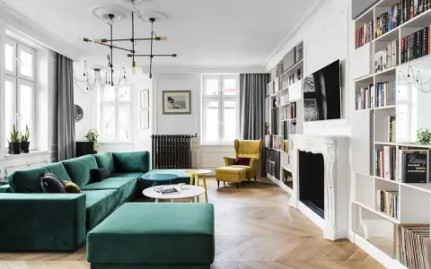 Elegancki salon w stylu paryskim z zieloną kanapą, żółtym fotelem i regałami pełnymi książek.