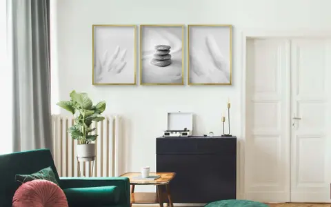 Trzy minimalistyczne plakaty w złotych ramach nad ciemną komodą. Dowiedz się, jak powiesić plakat bez niszczenia ścian.