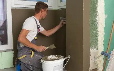 Budowlaniec tynkuje krzywą ścianę w przedpokoju.