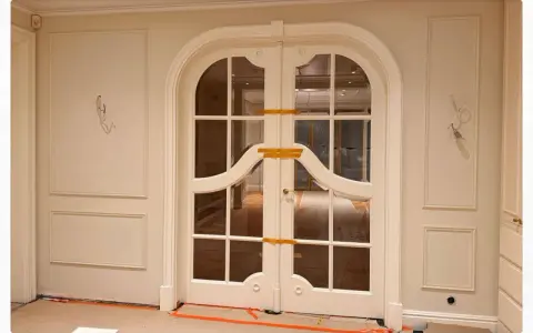 Elegancka sztukateria zdobi ściany korytarza, prowadząc do dwuskrzydłowych drzwi z łukiem i ozdobnymi szprosami.