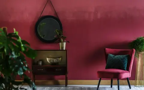Elegancki salon z burgundowymi ścianami, aksamitnym fotelem i stylową komodą.