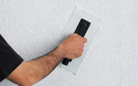Ręka z kielnią wygładza tynk na styrodurze. Dowiedz się, jak wykończyć styrodur, by uzyskać gładką ścianę.