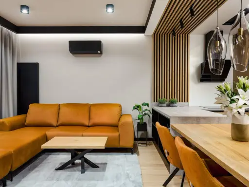 Nowoczesny salon bez sufitu z pomarańczową kanapą, drewnianym stołem i designerskimi lampami.
