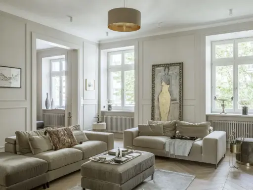 Elegancki salon z dwoma beżowymi sofami, ozdobną sztukaterią na ścianach i dużym obrazem.