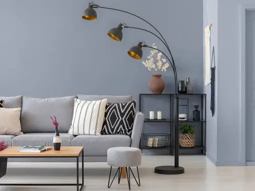 Przytulny salon z szarą kanapą, stolikiem kawowym i łukową lampą. Ciepły szary kolor ścian tworzy relaksującą atmosferę.