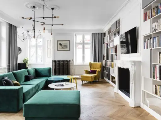 Elegancki salon w stylu paryskim z zieloną kanapą, żółtym fotelem i regałami pełnymi książek.