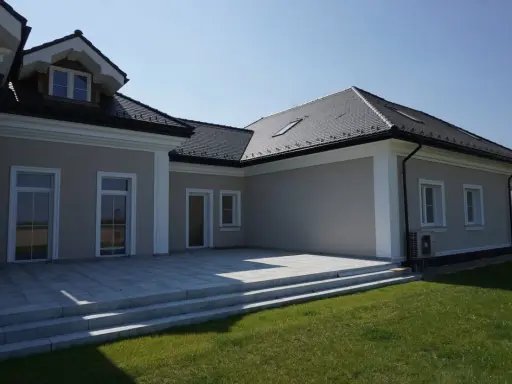 Nowoczesny dom z tarasem i trawnikiem. Elegancki gzyms co to? To ozdobny element architektoniczny podkreślający linię dachu.