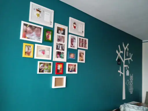 Galeria zdjęć na turkusowej ścianie, z motywem drzewa i lisa po prawej stronie.