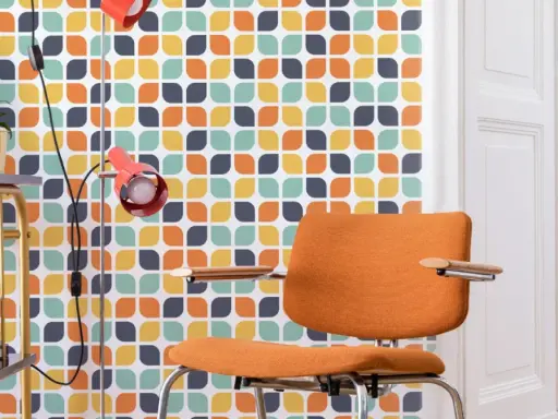 Pomarańczowe krzesło i lampa na tle tapety z geometrycznym wzorem w stylu retro.