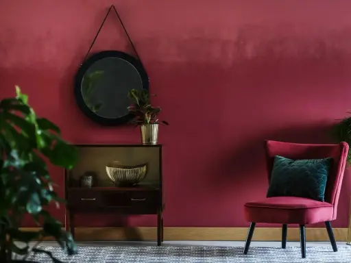 Elegancki salon z burgundowymi ścianami, aksamitnym fotelem i stylową komodą.