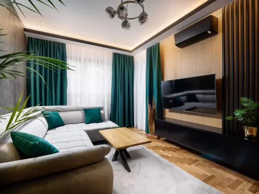 Nowoczesny salon z szarą kanapą i zielonymi poduszkami. Po prawej stronie ściana ozdobiona pionowymi lamelami w narożniku, na niej telewizor.