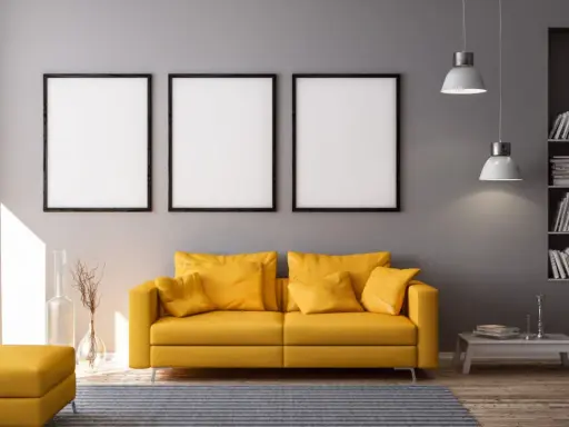 Nowoczesny salon z żółtą kanapą i trzema pustymi ramkami nad nią. Idealne miejsce, by dowiedzieć się, jak powiesić 3 obrazy na ścianie.